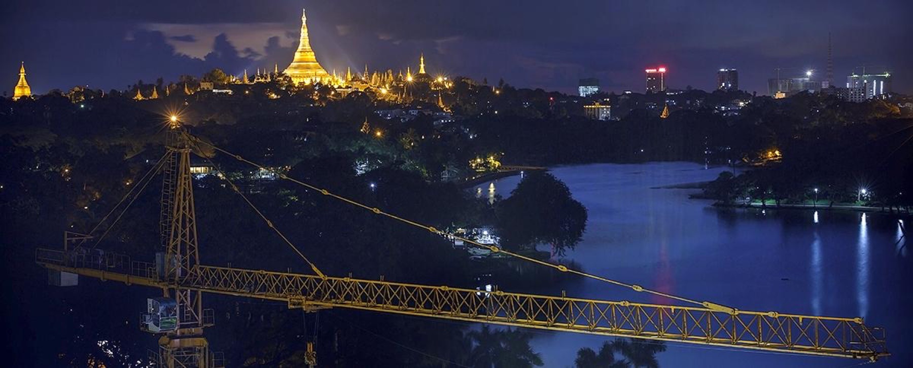 Shwedagon Pagoda at night over Kandawgyi Lake, Yangon, with a construction crane in the foreground